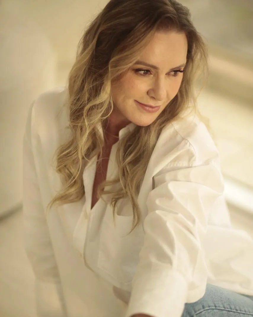 Patrícia Sivieri de camisa branca, sentada, sob luz natural