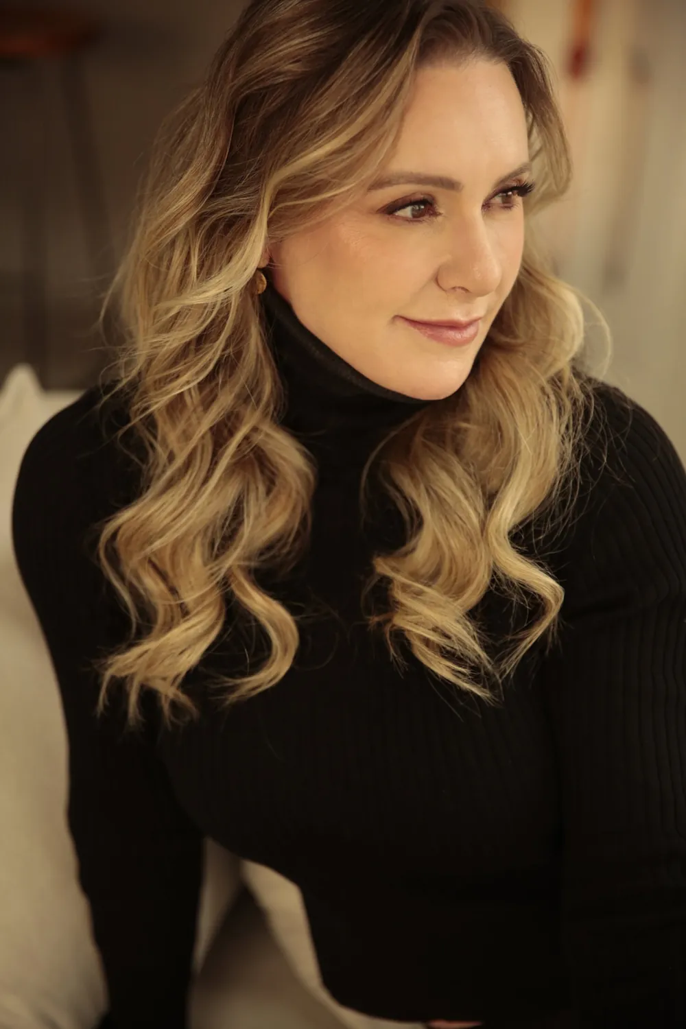 Patrícia Sivieri de blusa preta de gola alta, olhando para o lado